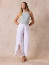 Pantalón blanco de lino con pretina ancha elastizada en punto smock, pierna ancha y ruedo con tajo.