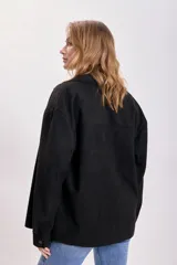 Sobrecamisa negra de antelina con cuello clásico, cierre frontal con botones, dos bolsillos de parche en el pecho y corte holgado.