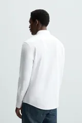Camisa celeste a rayas verticales blancas, de corte recto, con cuello italiano abierto, mangas largas con puños abotonados y cierre frontal con botones.