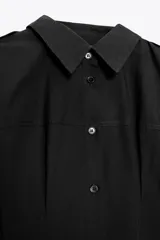 Vestido midi negro tipo gabardina, con cuello solapa, manga tres cuartos con puño y trabillas en el hombro, bolsillos laterales ocultos, pinzas y cierre frontal con botones.