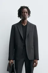 Blazer negro regular fit confeccionado en tejido de lana. Cuello con solapas de muesca y manga larga acabada en puño con botones. Bolsillos de vivo en pecho y de solapa en cadera. Detalle de bolsillo interior. Bajo con aberturas en espalda. Cierre frontal de botonadura.