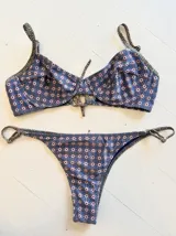Conjunto de bikini con estampado geométrico en tonos azul, blanco y marrón. El corpiño es de corte clásico con breteles finos y la bombacha es vedetina con tiras ajustables en los laterales.