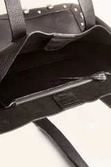 Bolso tote de cuero color marrón con doble asa de hombro y tachas plateadas en los laterales y la base. Incluye sobre interior de cuero.