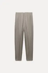 Pantalón tobillero color gris claro, de tiro alto, con bolsillos delanteros de vivo y cierre frontal con cremallera, botón interior y gancho metálico.