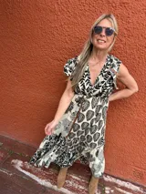Vestido largo de seda color crema con estampado de hojas y flores en negro. Tiene escote en V cruzado, mangas cortas con volados y lazo ajustable en la cintura.
