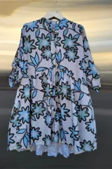 Vestido camisero con estampado floral en tonos celeste, azul y marrón. Tiene cuello mao, botones frontales, corte con volados y mangas tres cuartos.