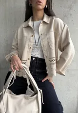Sobrecamisa color beige de gamuza sintética con cuello camisero, cierre frontal con botones dorados, bolsillos de parche en el pecho y bajo con calados.