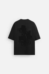 Camiseta negra de corte holgado, cuello redondo y manga corta. Estampado frontal con texto vertical y diseño geométrico abstracto en negro.
