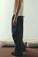 Pantalón cargo de algodón, color negro lavado, con corte holgado y cordón ajustable en cintura y tobillos. Presenta bolsillos cargo grandes en las piernas con solapas y pliegues cosidos en las rodillas.