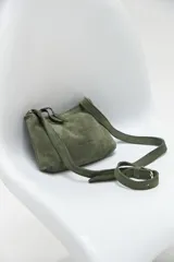 Bandolera pequeña de cuero gamuzado color verde oliva, con correa larga regulable y cierre superior con borla de cuero.