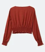 Blusa color ladrillo con escote redondo con ajuste, mangas largas con aberturas en los hombros y elástico en la cintura.