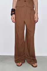 Pantalón marrón de tiro medio, confeccionado en mezcla de lino y viscosa. Presenta trabillas en la cintura, bolsillos laterales, pinzas y raya planchada en el delantero. Cierre frontal con cremallera, botón y ganchos metálicos.