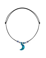 Collar con dije de luna creciente azul y verde, engarzado en un cordón de cuero negro con cuentas plateadas y azules.