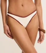 Conjunto de bikini blanco con ribete marrón en contraste. El corpiño es de corte triangular con detalle de argolla en el centro. La bombacha es de corte clásico con tiro medio.