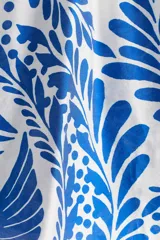 Blusa oversized con cuello elevado fruncido, abertura en V adelante y bajo recto. Mangas globo largas de corte raglán con abertura y botón en los puños. Estampado floral en tonos azules y blancos.