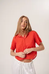 Camisa corta color rojo con broderie, cuello clásico, cierre frontal con botones, manga corta y bolsillo en el pecho.