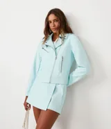 Chaqueta biker celeste de cuero sintético con cierre frontal asimétrico, cuello solapa con botones a presión y bolsillos con cremallera.