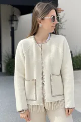 Chaqueta corta color gris oscuro confeccionada en lana merino hervida, con cuello redondo, mangas largas y bolsillos frontales. Presenta detalle de flecos en el ruedo.