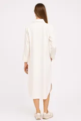 Túnica midi color beige de lino, corte holgado, manga larga, cuello camisero y cierre frontal con botones.