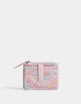 Billetera pequeña de cuerina estampada con flores de colores. Tiene cierre superior con tirador rosa, lazo con broche a presión y compartimentos para tarjetas.