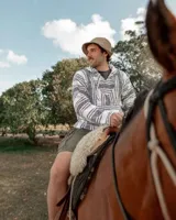 Buzo estilo mexicano con capucha, tejido en hilo grueso a rayas horizontales blancas y negras, con bolsillo tipo canguro y cordones ajustables en el cuello.