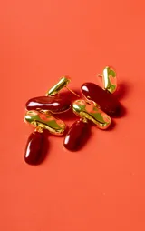 Aros colgantes con diseño de tres piezas: una pieza superior dorada irregular, una pieza central ovalada color bordó, una pieza intermedia dorada con textura y una pieza inferior alargada color bordó.