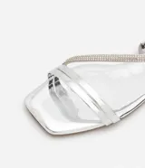 Sandalia plana plateada con tiras finas y detalles de strass, puntera cuadrada y cierre con hebilla en el tobillo.