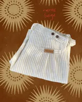 Pantalón de lino beige con rayas verticales blancas, corte recto, tiro medio, bolsillos laterales y cierre con botón y presillas para cinturón.