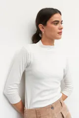 Polera de algodón blanca de cuello alto, con mangas 3/4 y costuras delicadas en las sisas.