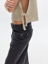 Chaleco de punto color beige con cuello alto y pechera desmontable con flecos.