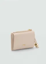Monedero pequeño color beige con efecto piel y detalle de abalorios. Tiene cierre de solapa con botón magnético, bolsillo interior y bolsillo lateral con cierre de cremallera.