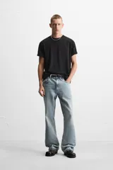 Pantalón de jean negro con efecto lavado, corte flare, cinco bolsillos, cierre frontal con cremallera y botón, y bajo con acabado irregular.