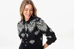 Camisa negra de lino con bordados florales blancos, de corte clásico, cuello camisero y mangas largas con puños abotonados.