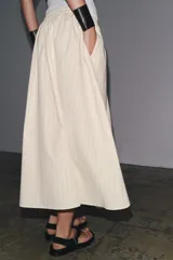 Falda midi de Zara Woman Collection confeccionada en hilatura de algodón color crudo con finas rayas verticales marrones. Tiene tiro medio, cintura elástica ajustable con cordones y bajo evasé.