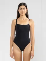 Traje de baño enterizo negro con breteles finos y detalle de cadena dorada en uno de los hombros.