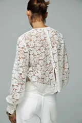 Top de encaje blanco con cuello redondo, mangas largas abullonadas y puños con botones metálicos.