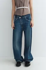 Jeans de tiro medio color azul denim, corte baggy, con trabillas y cinco bolsillos. Cierre frontal asimétrico con cremallera y botones metálicos.