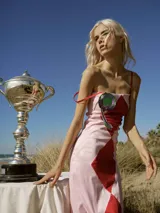 Vestido midi de breteles finos, color rosa con rombos rojos y detalle de roseta en el pecho. Silueta ajustada al cuerpo y largo asimétrico.