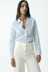 Camisa celeste con rayas verticales en blanco y amarillo, de corte entallado, cuello solapa y manga larga.