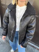 Campera negra estilo aviador, con cuello y forro de piel sintética. Cierre frontal con cremallera y hebilla en el cuello. Bolsillos laterales con solapa y puños ajustables con hebilla.