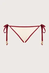 Calzón de bikini color blanco marfil, con ribete rojo oscuro y tiras laterales con detalle de piedras doradas.