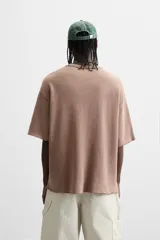 Camiseta color marrón claro con cuello redondo, mangas cortas y estampado frontal con texto e imagen en blanco.