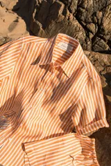 Camisa de lino a rayas verticales color naranja y blanco, de manga corta y corte oversize. Presenta bordados con motivos playeros en el frente y la espalda.