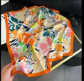 Pañuelo cuadrado de tela con estampado floral multicolor y borde naranja.