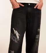Pantalón masculino super baggy confeccionado en jeans sostenible con cintura con trabilla, cierre tradicional, bolsillos y estampa de grafiti.
