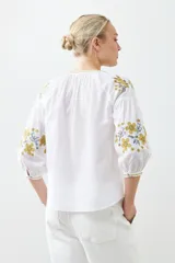 Blusa blanca de estilo boho con bordados de flores en amarillo y azul en mangas y escote.