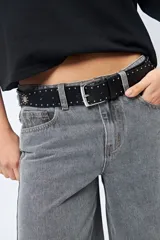 Cinturón negro de cuero sintético con hebilla metálica plateada y apliques de tachas plateadas con forma de corazón y circulares.