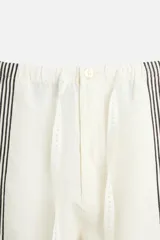 Pantalón relaxed fit confeccionado en tejido de lino color crudo. Cintura elástica ajustable con cordón, bolsillos laterales y traseros. Perneras con aplicación de bandas verticales negras a contraste en delantero.