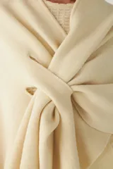 Ruana color crema de tejido de punto industrial con terminación en contraste de color. Tiene doble ojal para mantener el cruce.