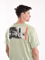 Remera verde claro de corte recto y mangas cortas, con estampado pequeño de palmeras y sol en el pecho.